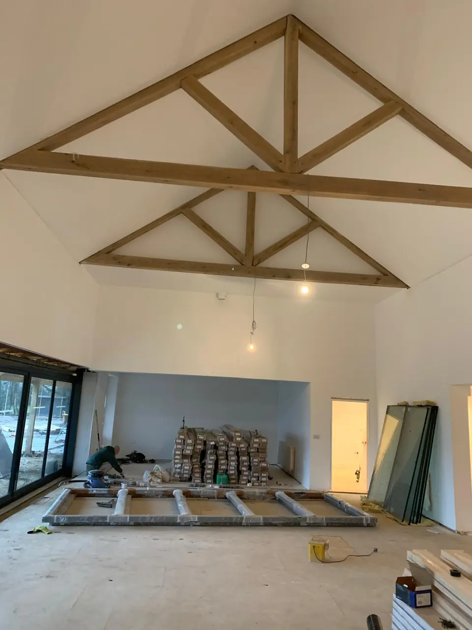 Large room with plastered walls beneath exposed timber roof trusses, during fit-out