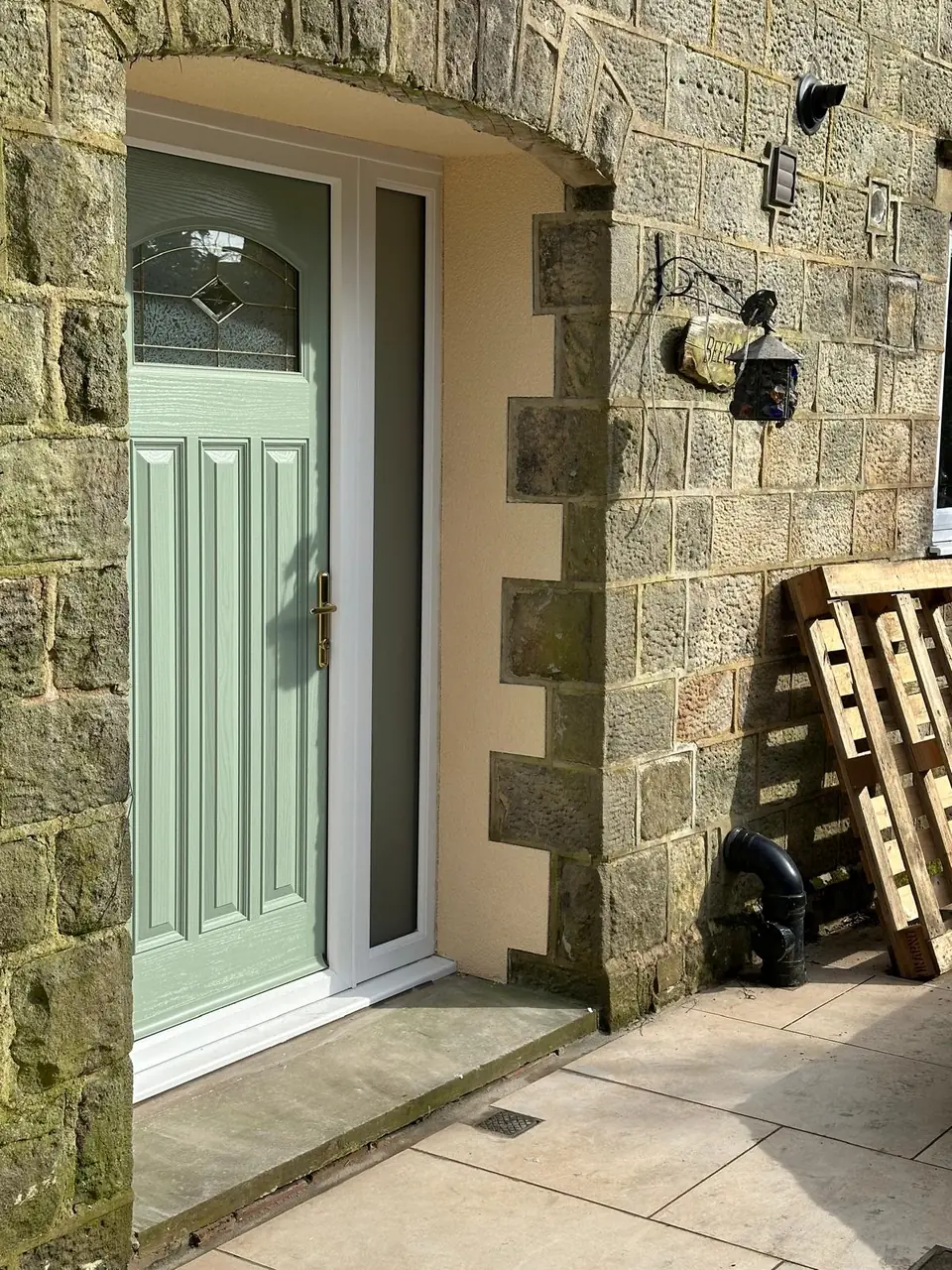 Green front door set in a stone wall, with cream render around the opening and stone quoins left exposed