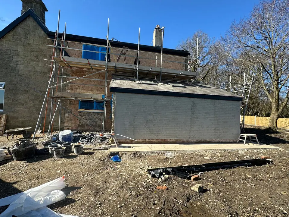 Stone house with scaffolding and a single-storey extension in a grey base coat, before the finish coat