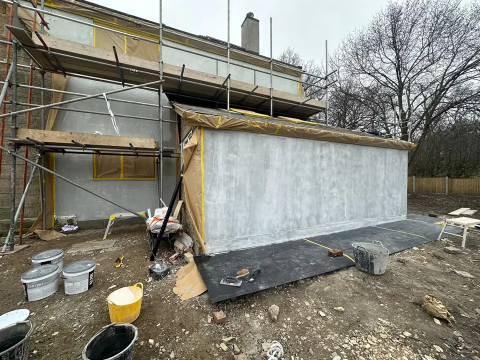 Single-storey extension beside a stone house, with its walls in a grey base coat and scaffolding still up