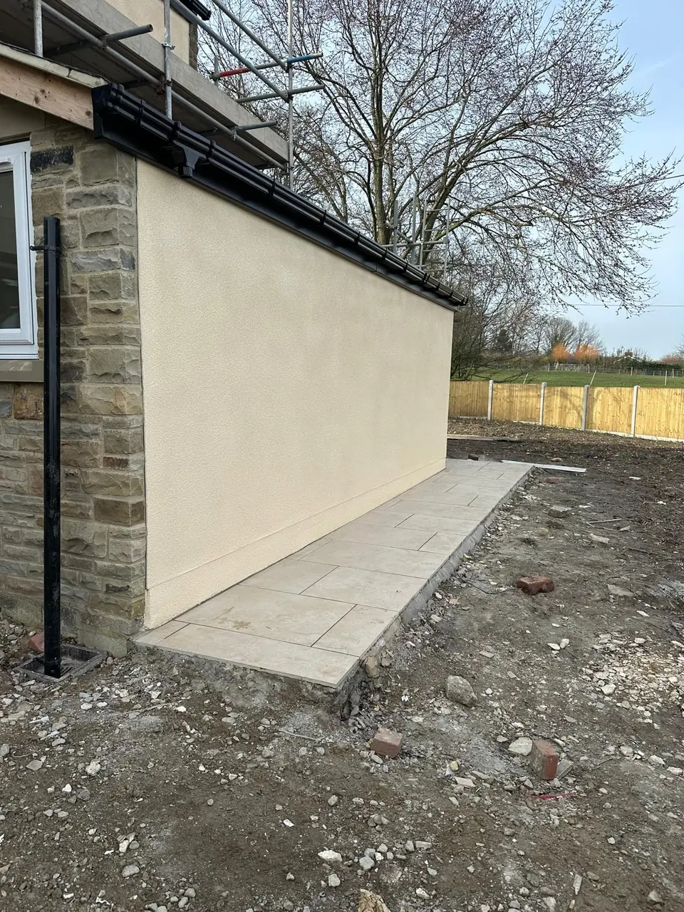 Long side wall of the extension in cream render, meeting the stone house and a new paved path