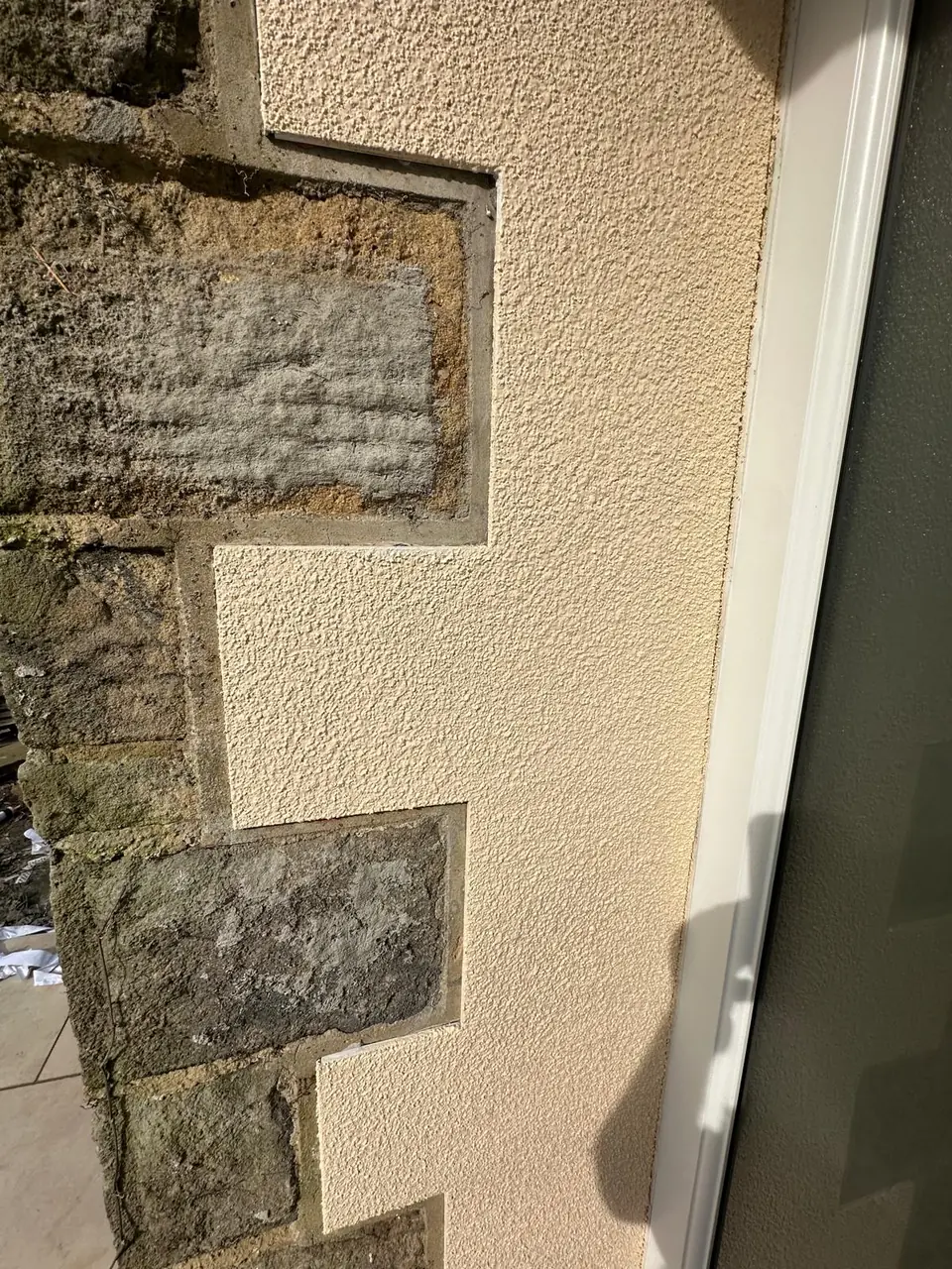 Close-up of cream textured render cut neatly around exposed stone quoins beside a white door frame