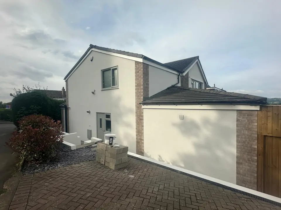 Side of the house in white render beside a block-paved driveway, with brick detailing at the corner